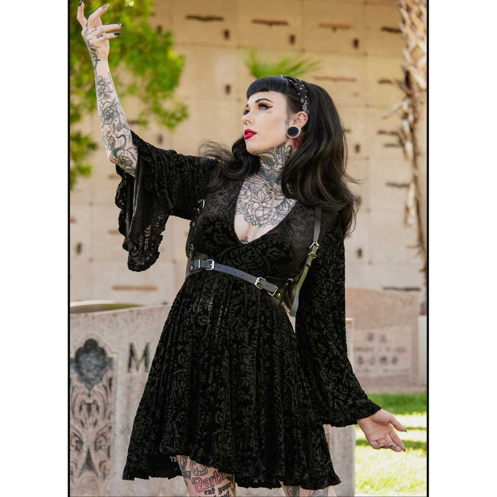 Woman in a black lace dress with tattoos and piercings, standing outdoors.