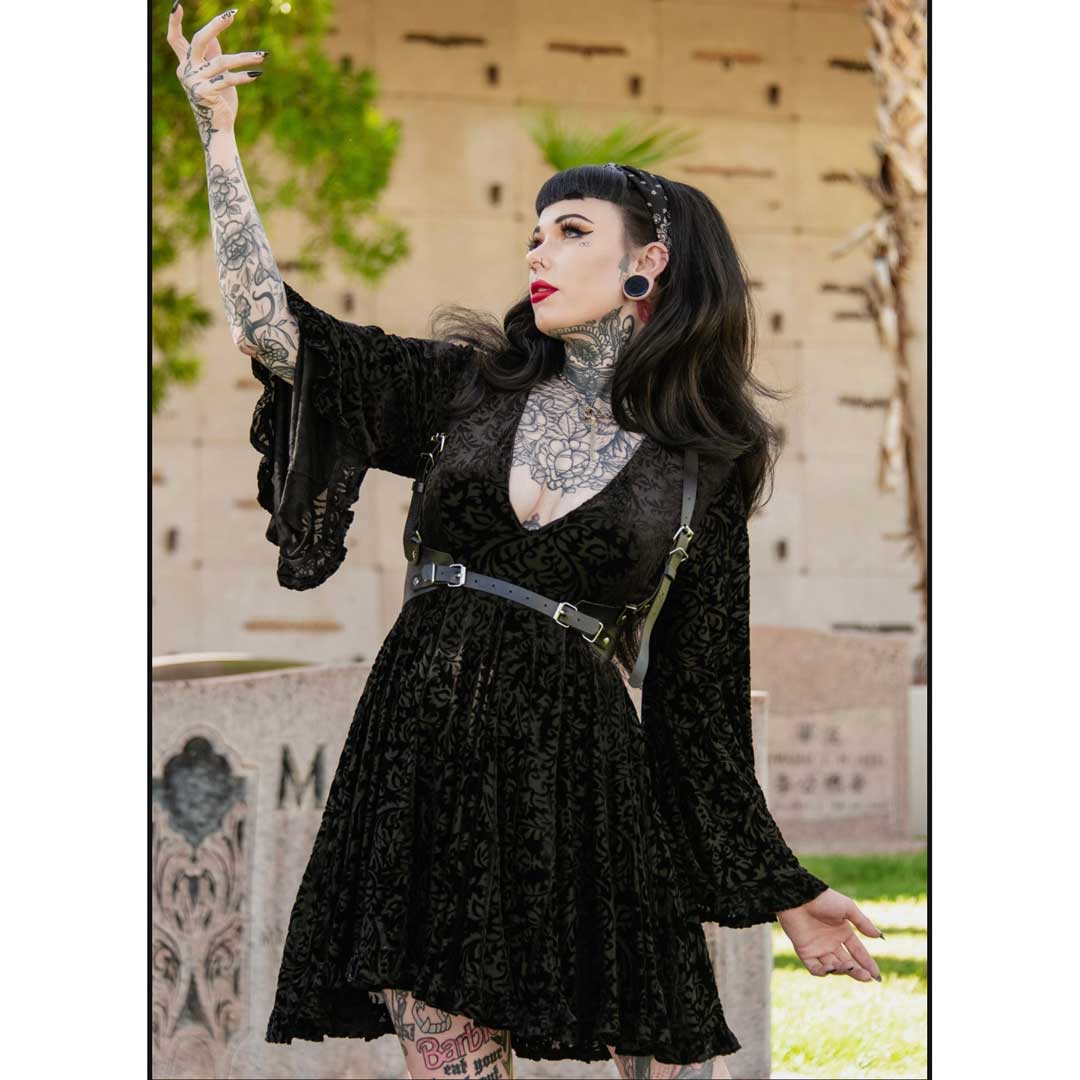 Woman in a black lace dress with tattoos and piercings, standing outdoors.