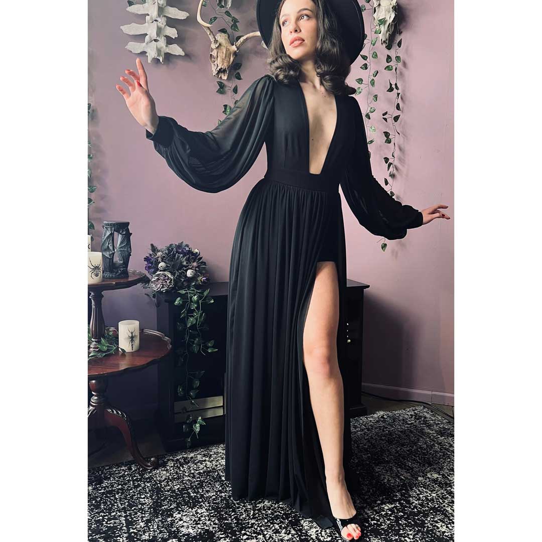 Woman in a black dress with a deep neckline and long sleeves standing in a room with decorative elements.