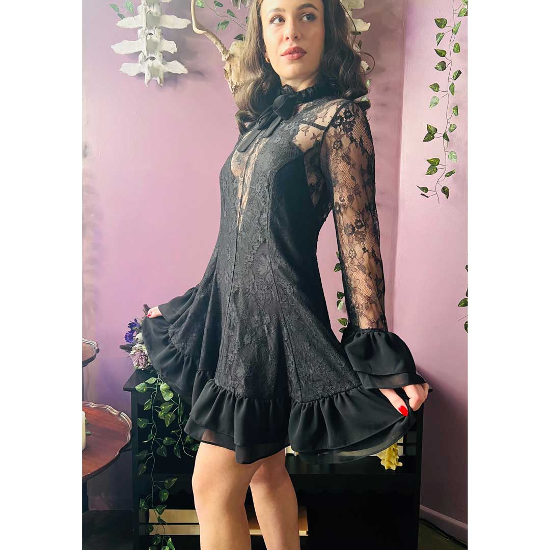 Woman wearing a black dress with lace sleeves in a room with pink walls and plants.