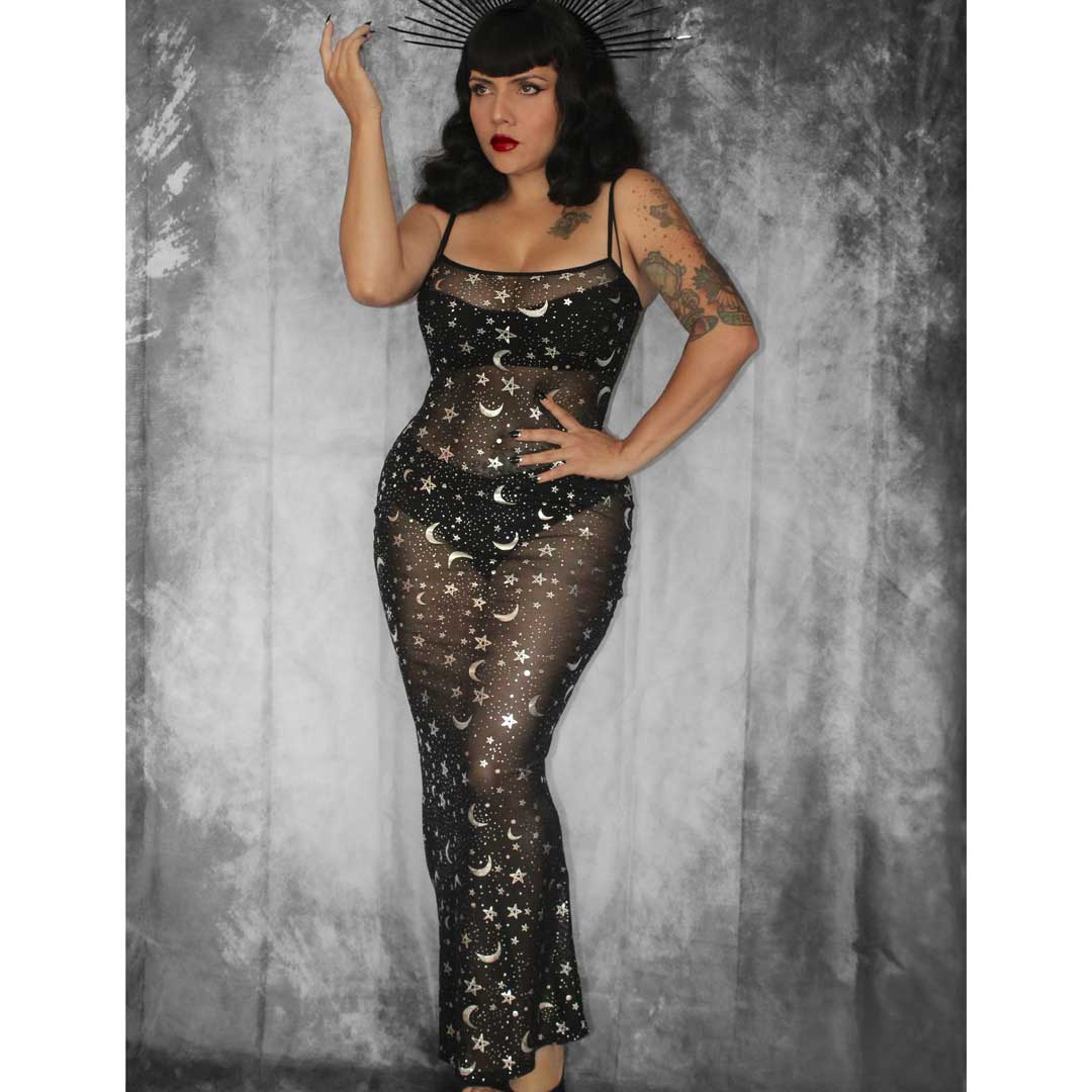 Woman wearing a black sheer dress with celestial designs against a textured gray background