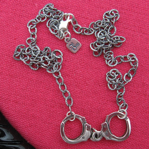 Silver chain bracelet with handcufflinks on a pink background