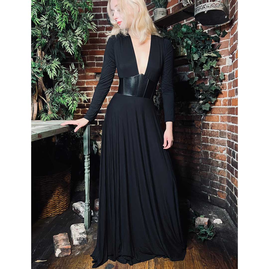 Woman in a black evening gown standing against a brick wall with decorative plants.