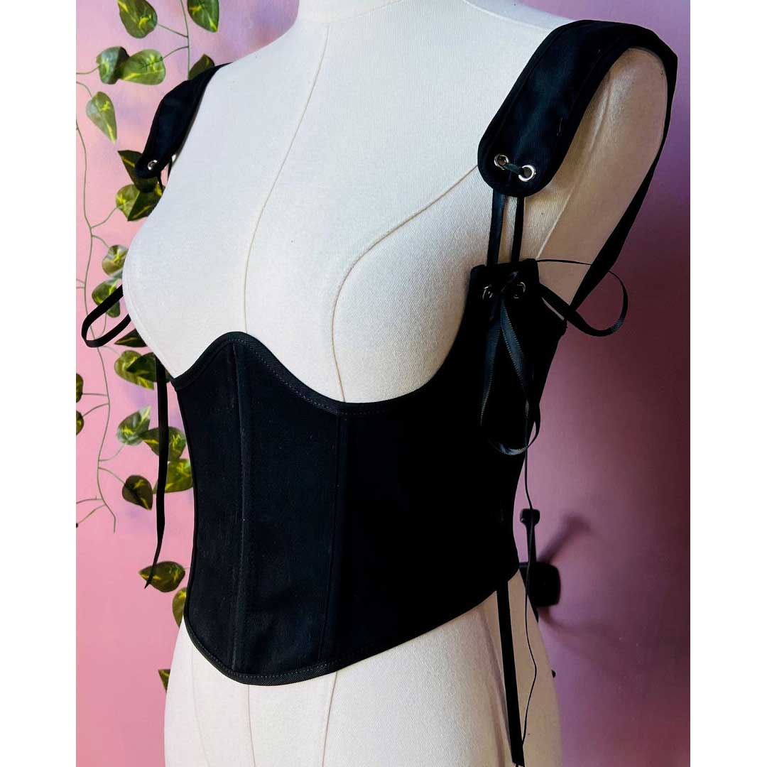 Black corset on a mannequin against a pink background with green leaves.