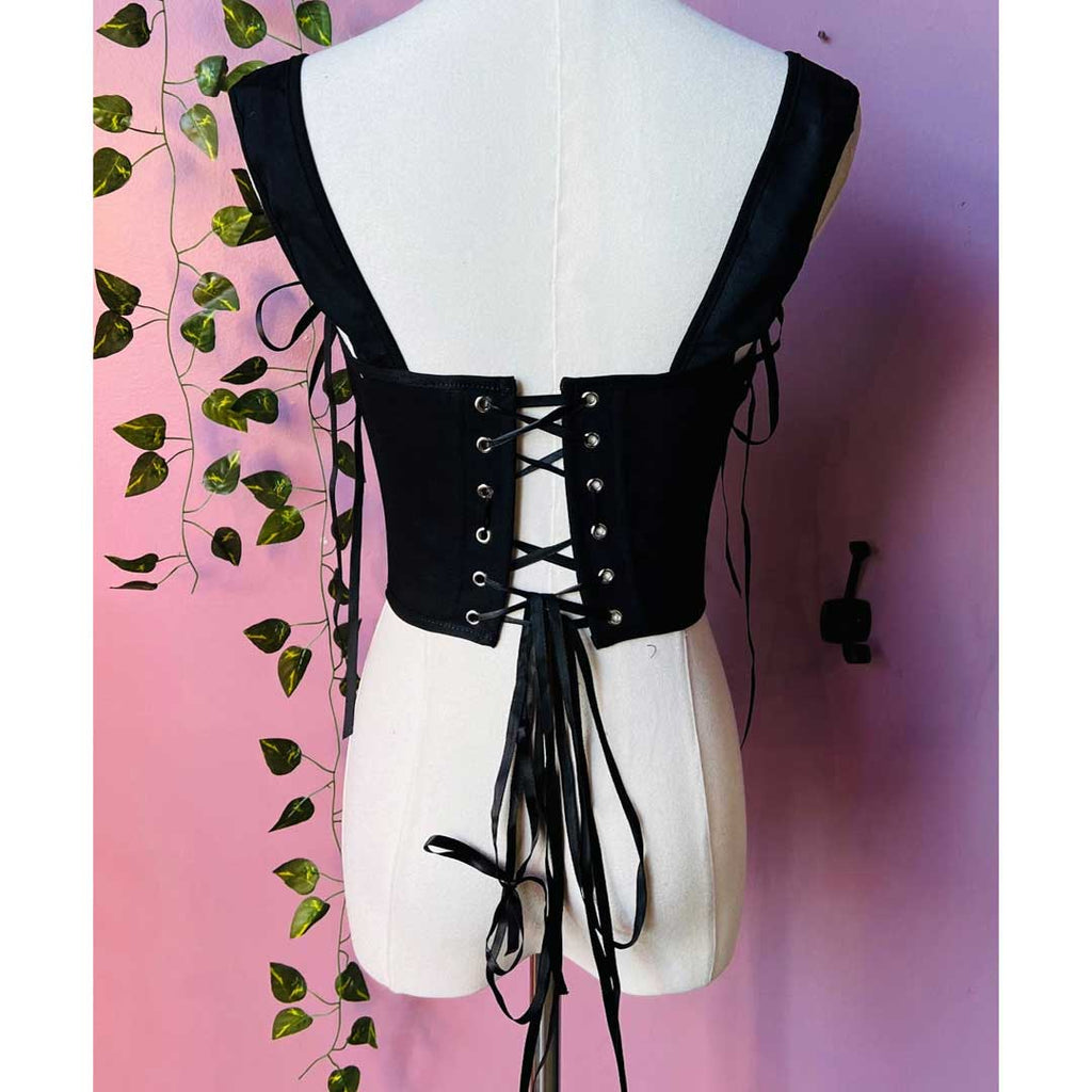 Black lace-up top on a mannequin against a pink background with green leaves.
