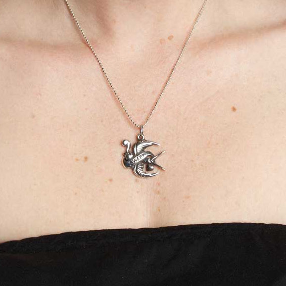 Person wearing a necklace with a unique pendant, surrounded by tattoos on arms and shoulders.