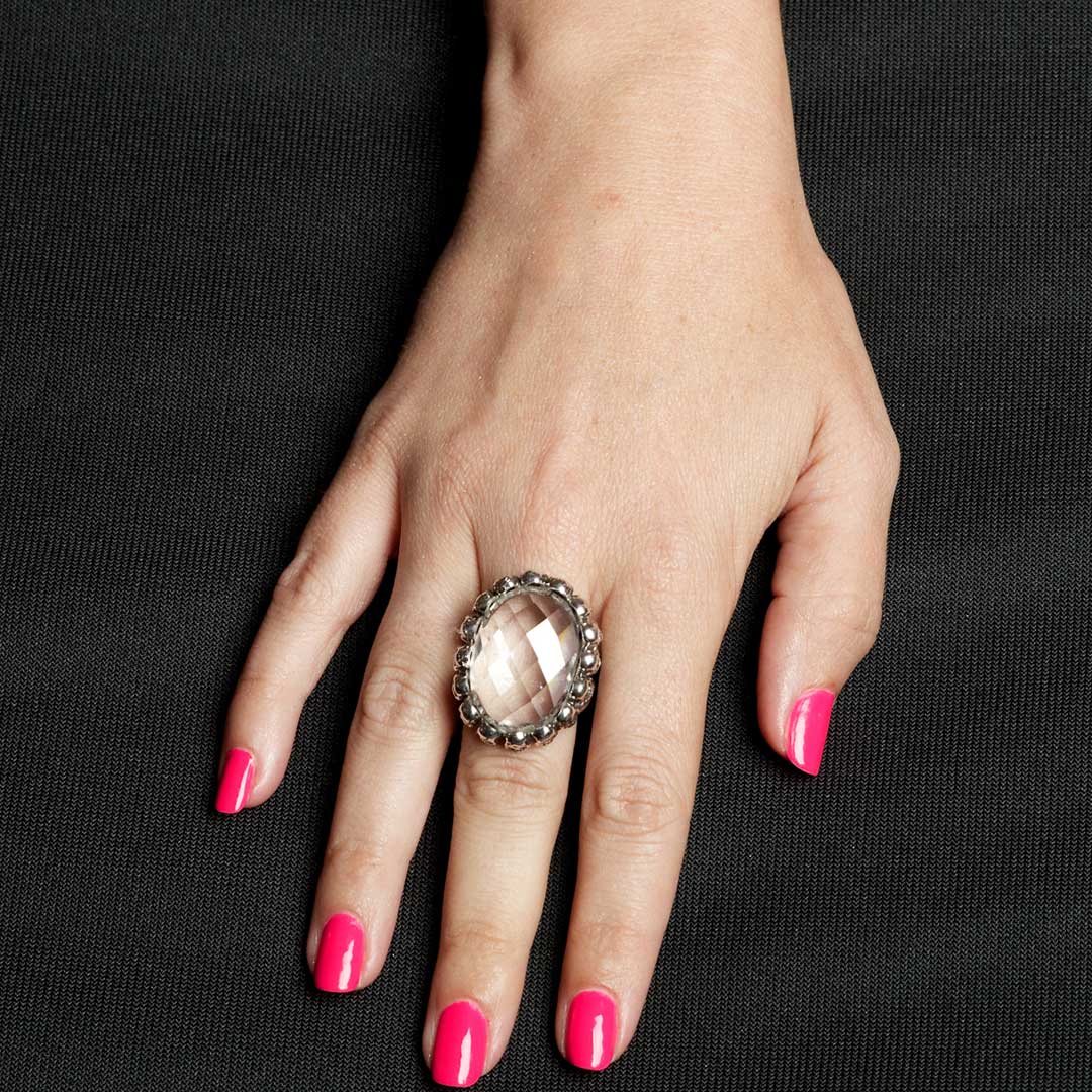 Hand wearing a decorative ring with pink nail polish on a black background
