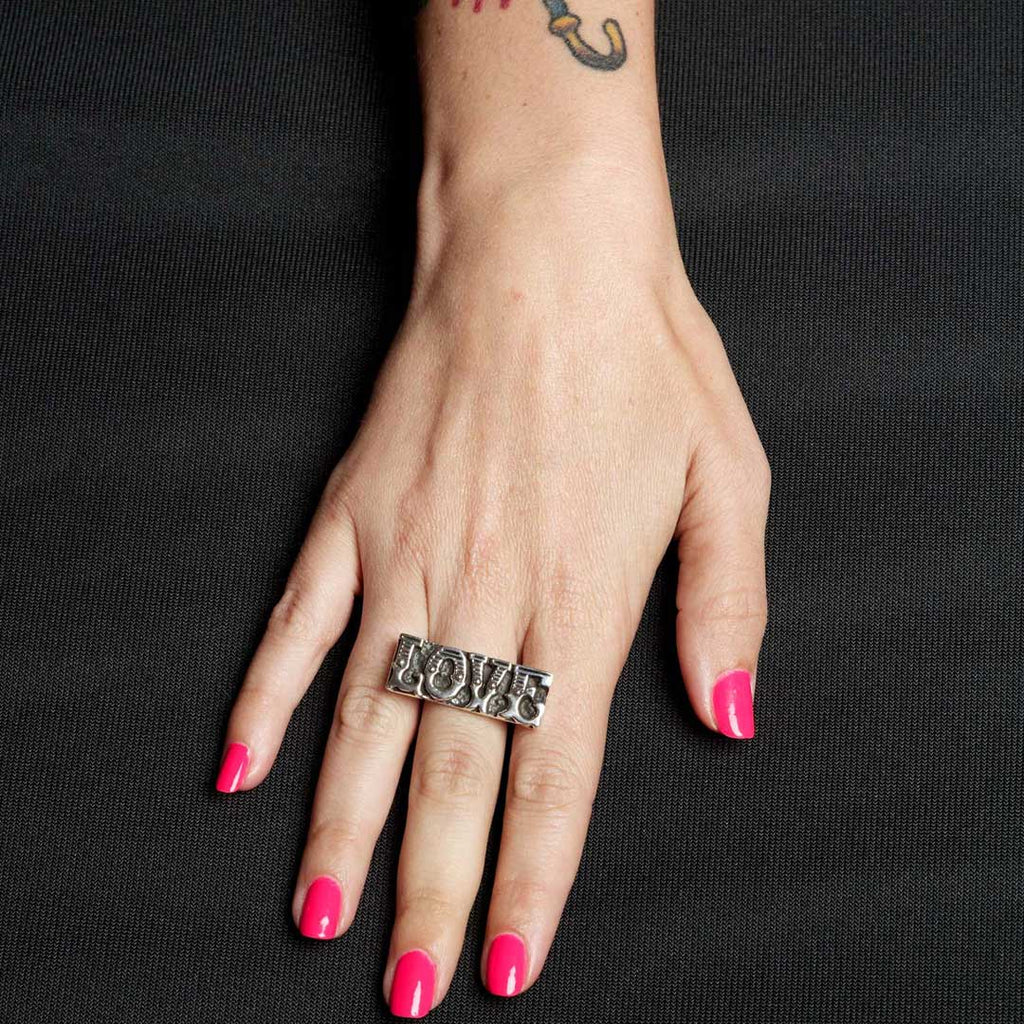 Hand wearing a silver ring with 'LOVE' on a black background