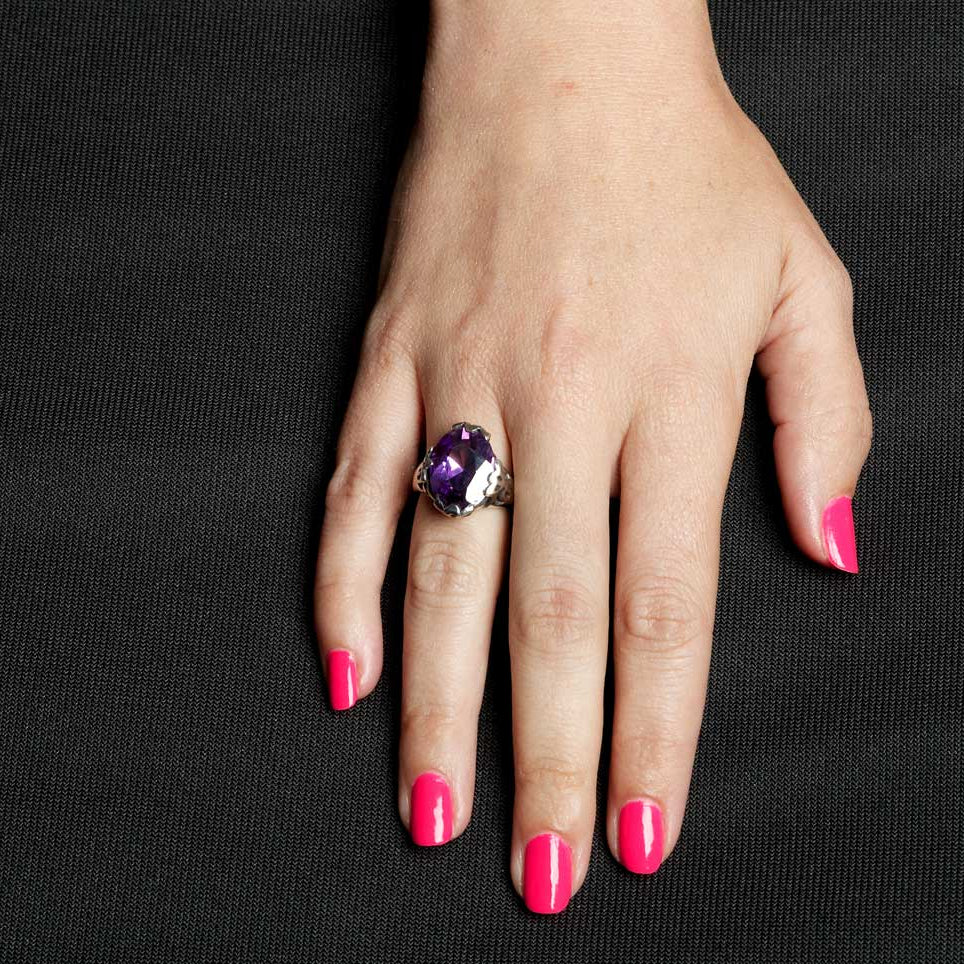Hand wearing a ring with a purple gemstone on a black background