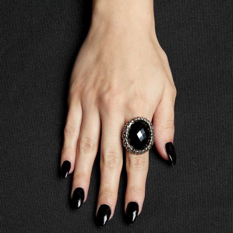 Hand wearing a black ring with a large gemstone on a dark background