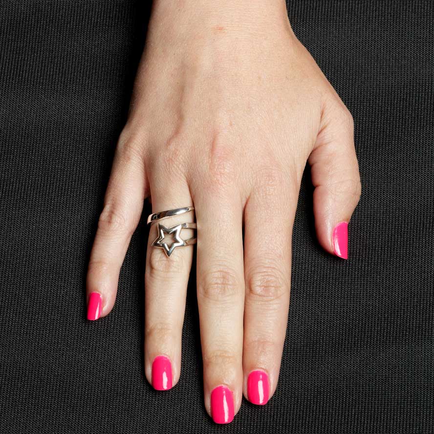Hand with pink nail polish wearing a silver star ring on a black background
