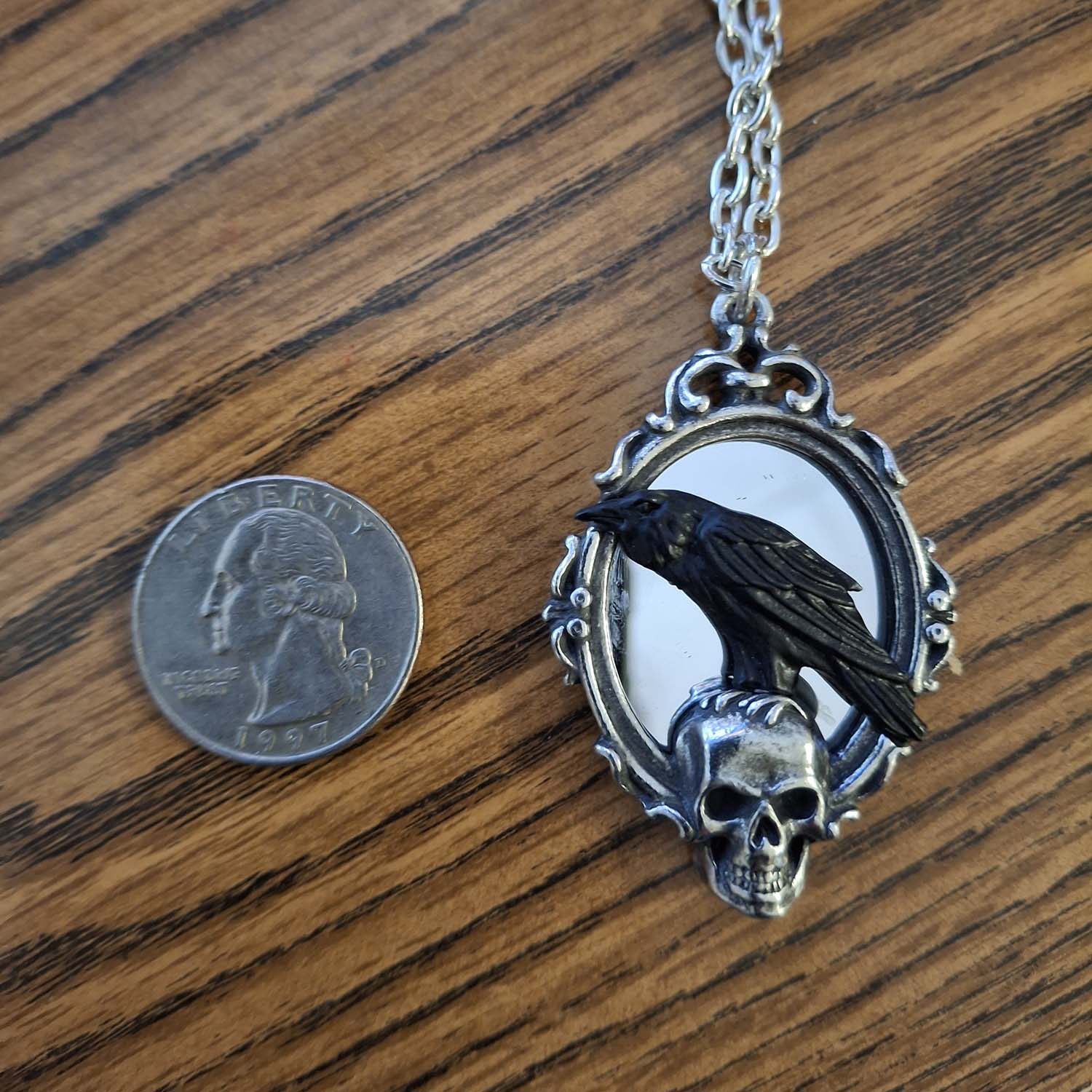 Pendant with a raven and skull design next to a quarter on a wooden surface