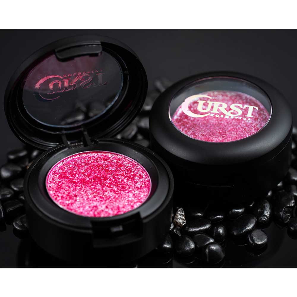 Two open makeup compact cases with pink glittery powder on a dark background, featuring the brand 'Curst'.