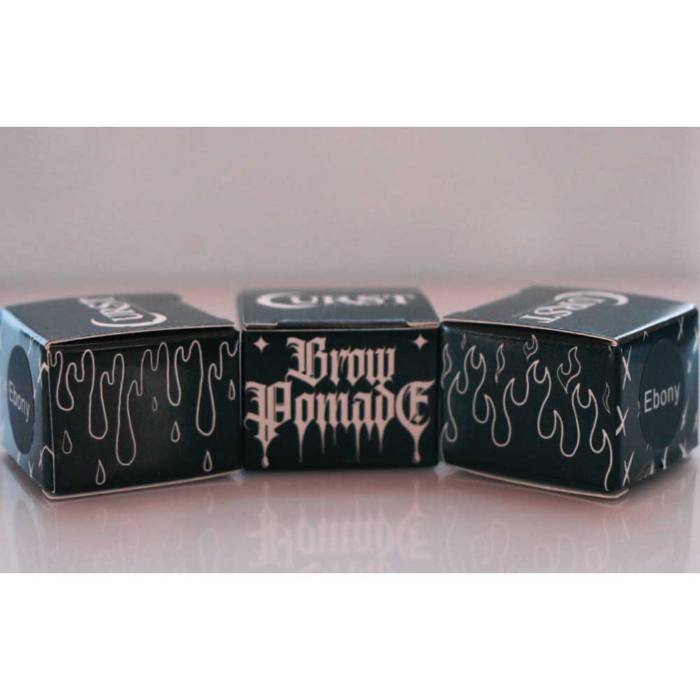 Three boxes of 'Brow Pomade' with 'Ebony' branding on a reflective surface.