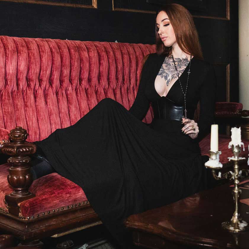 Woman in a black dress sitting on a red velvet couch with candles and a mirror in the background.