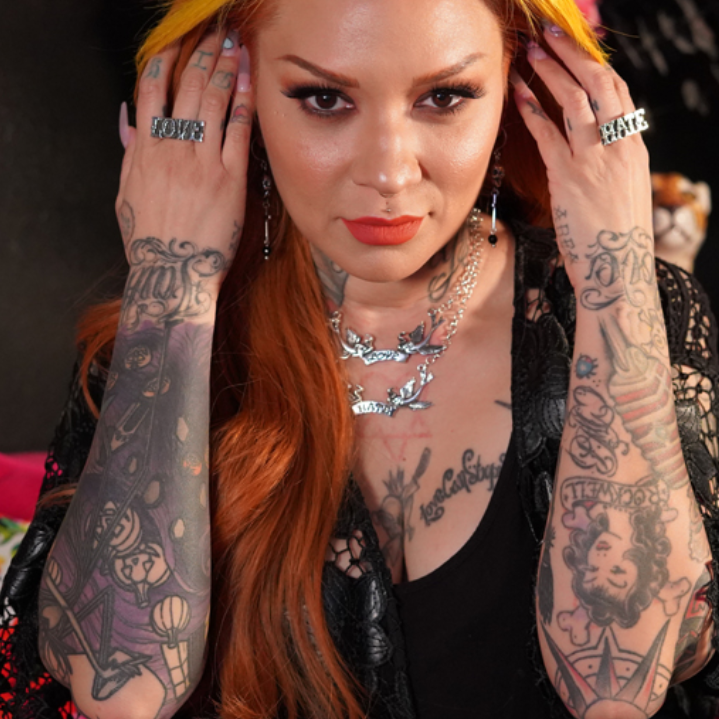 Woman with tattoos on arms and neck, wearing a black outfit.
