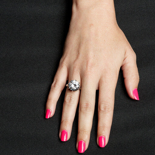 Hand with pink nail polish wearing a ring on a black background