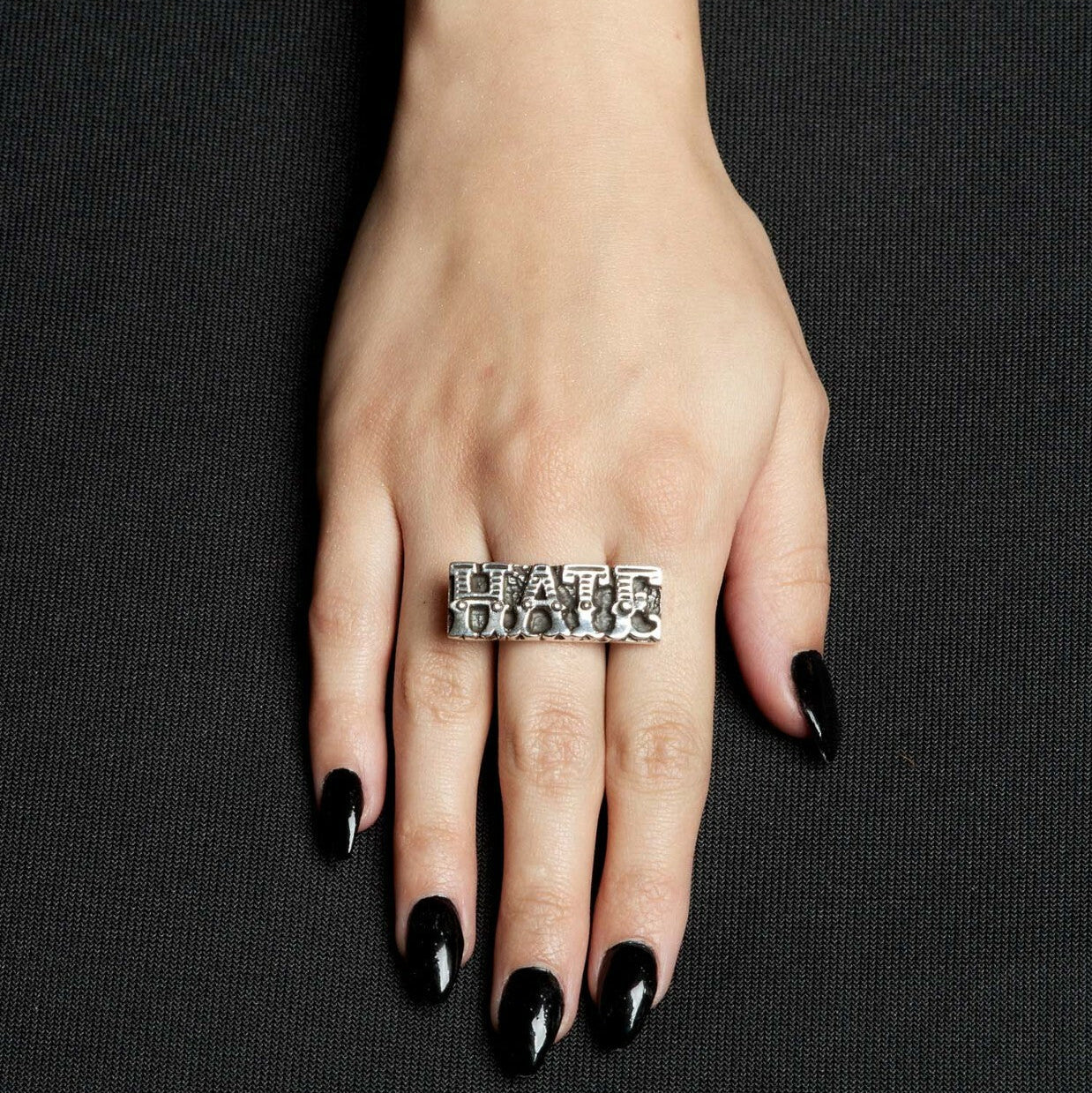 Hand wearing a silver ring with text on a black background