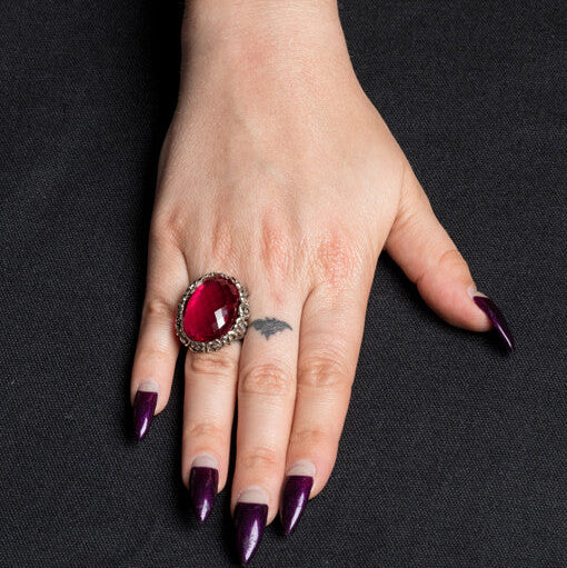 Hand wearing a large red gemstone ring on a black background