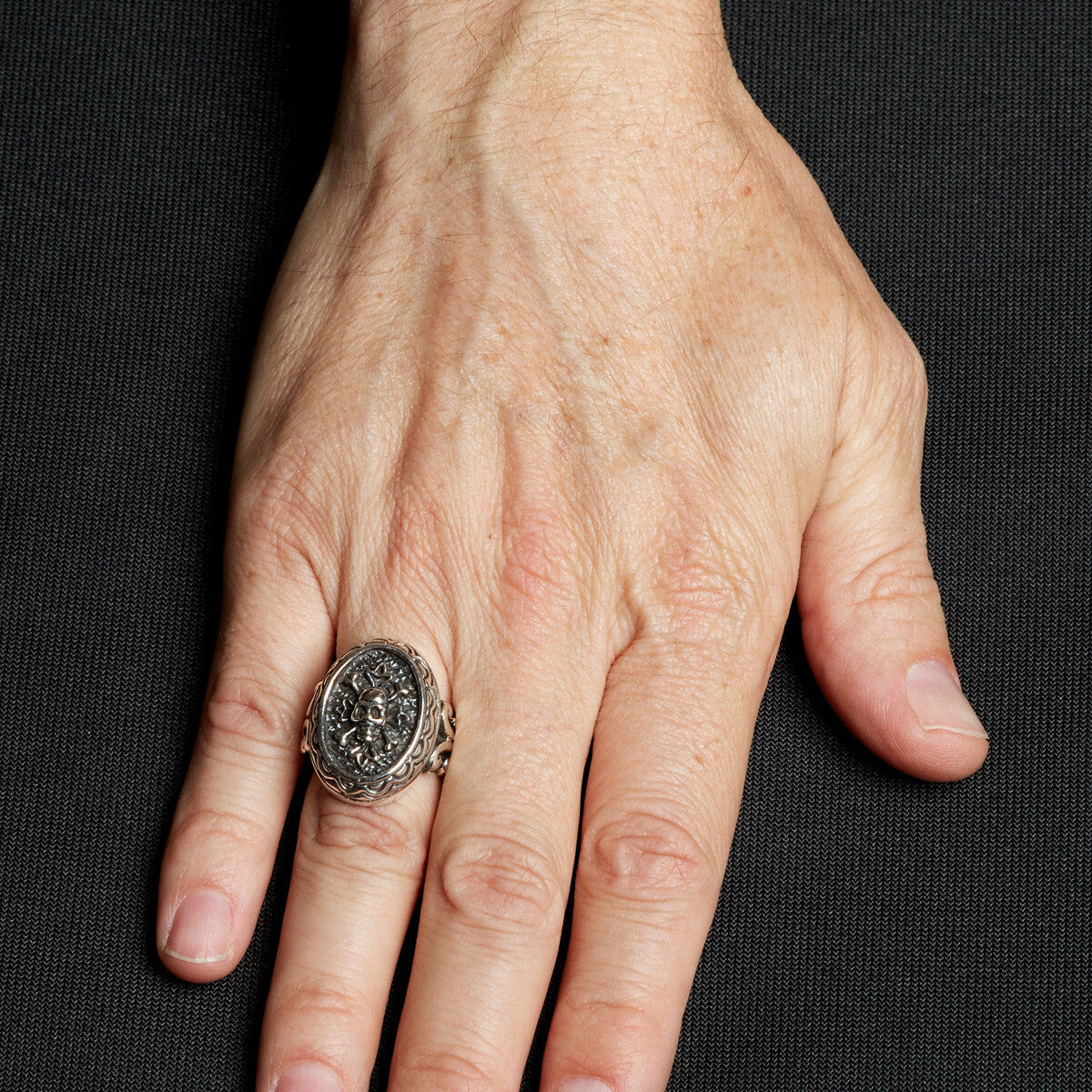 Hand wearing a silver ring with a black stone on a black background