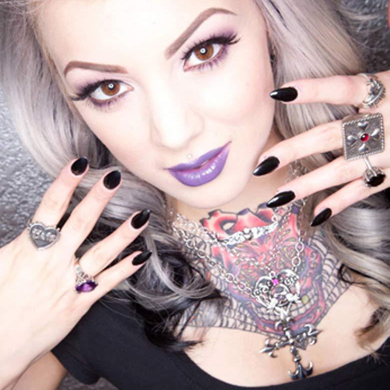 Close-up of a person with tattoos, purple lipstick, and multiple rings on fingers.