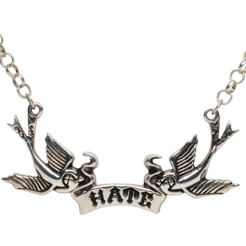 Silver necklace with two birds perched on a branch with the word 'HATE' below on a white background