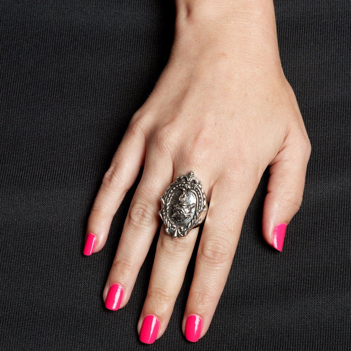 Hand wearing a silver ring with pink nail polish on a black background