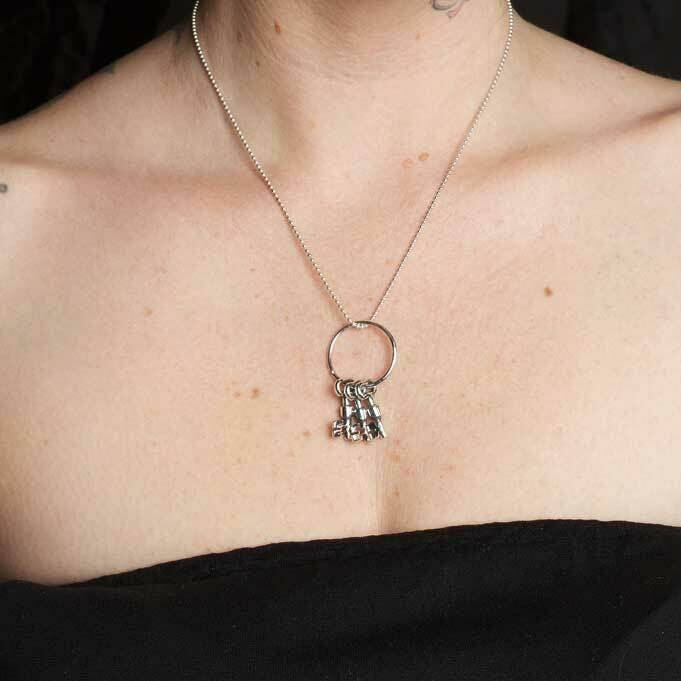 Person wearing a necklace with a pendant, showing tattoos on arms and chest.