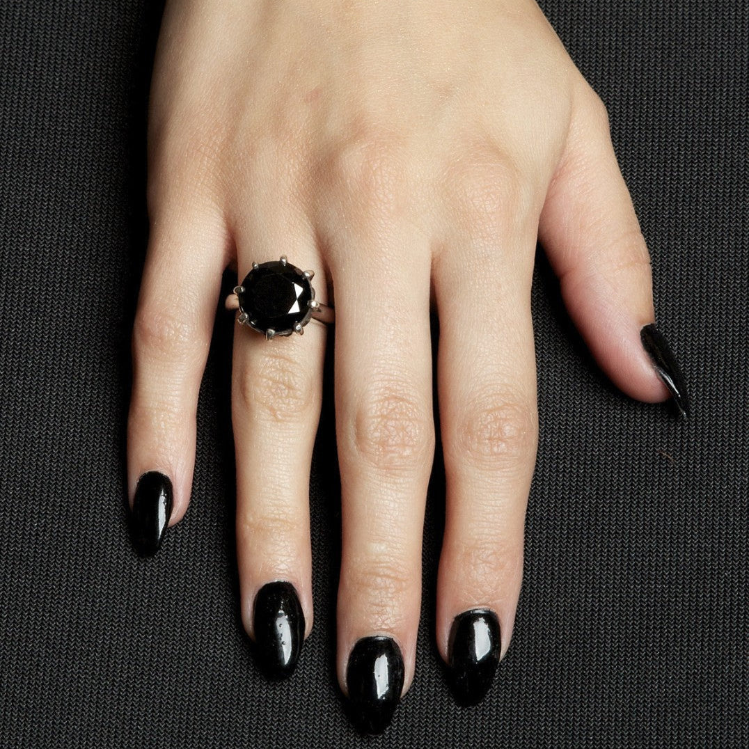 Hand with black nail polish wearing a black ring on a dark background