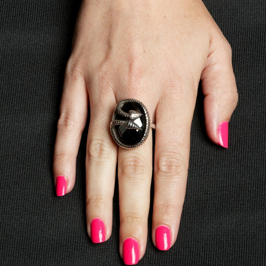 Hand with a black ring and pink nails on a black background