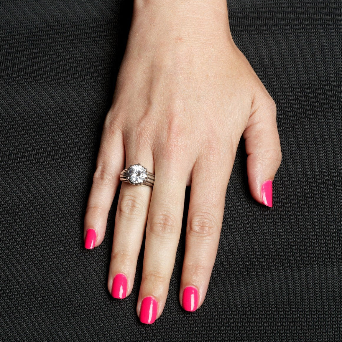 Hand with pink nail polish wearing a ring on a black background